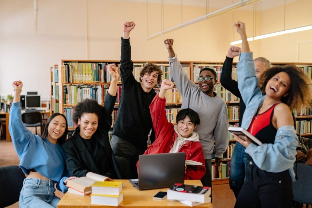 A group of happy students raising their hands near a wooden table in a library