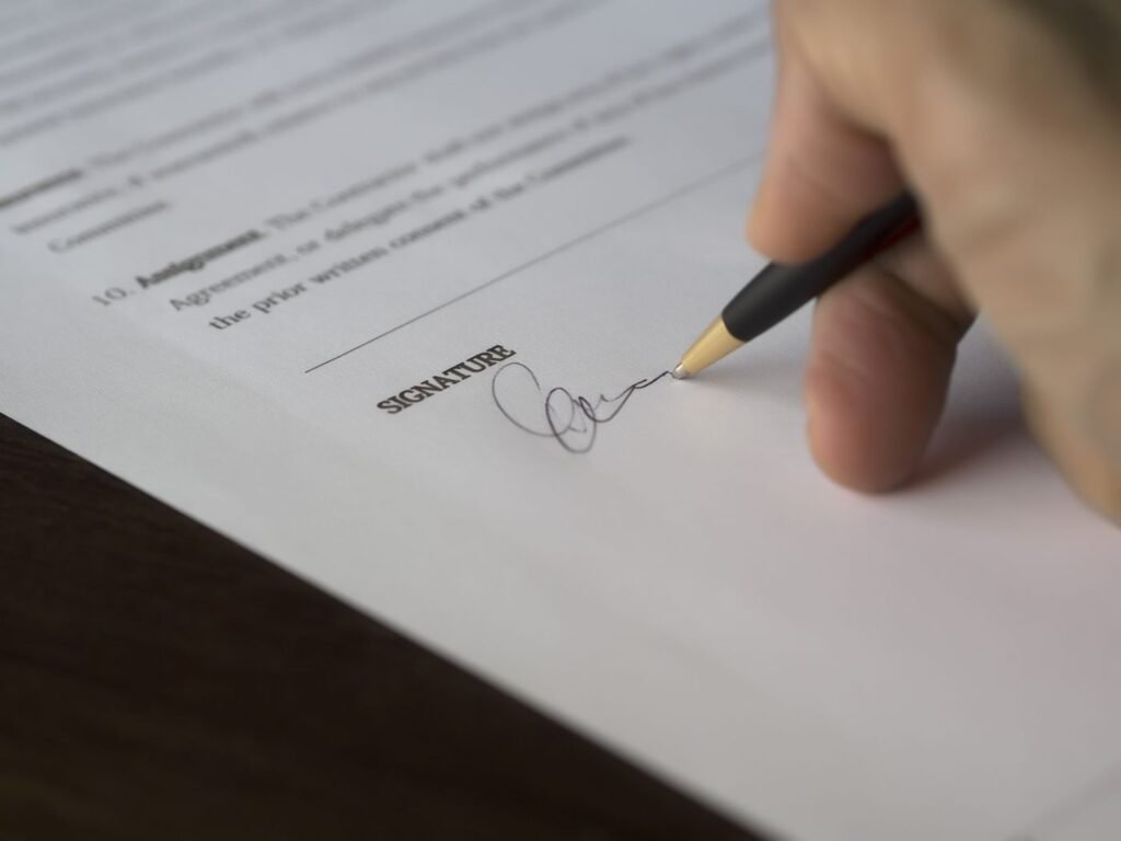 Hand signing a formal agreement with a pen on a wooden desk
