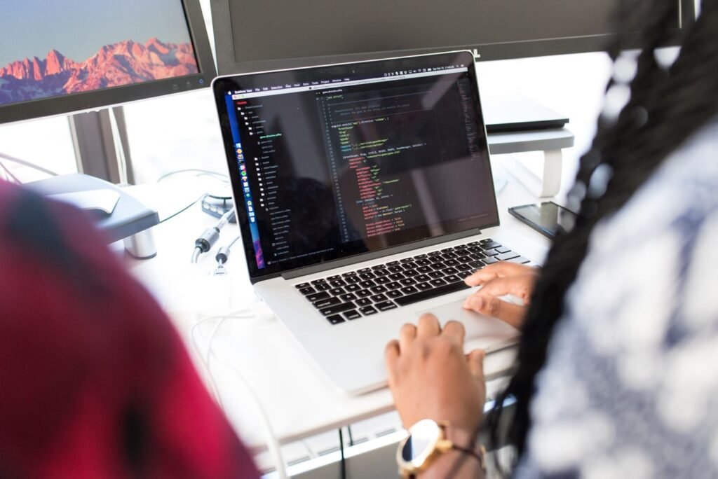 Woman writing code on a laptop in an office with several monitors