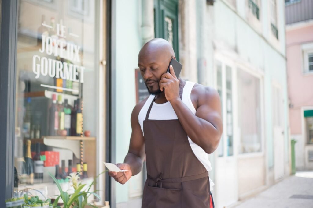 Shopkeeper in an apron on a phone call outside his store