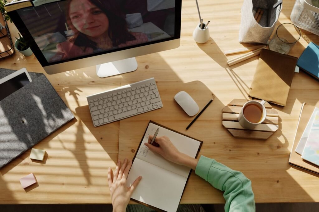 A student writing notes in a notebook during an online lesson at home
