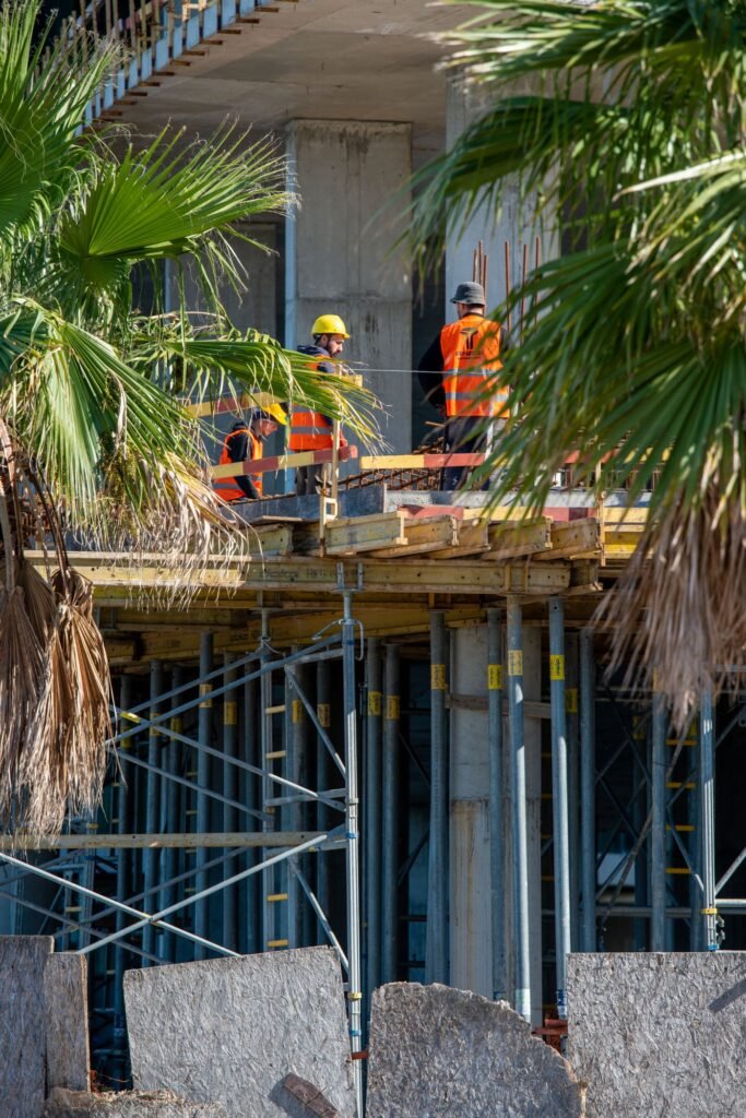 Construction workers in safety vests on scaffolding, with palm trees in front
