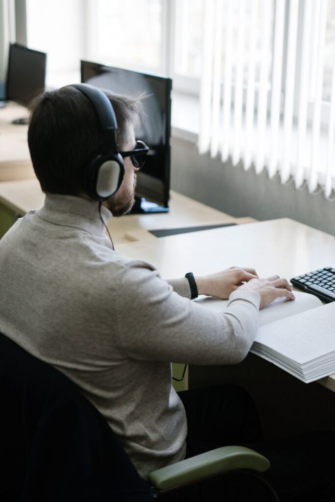 A visually impaired man reading a braille book while wearing headphones