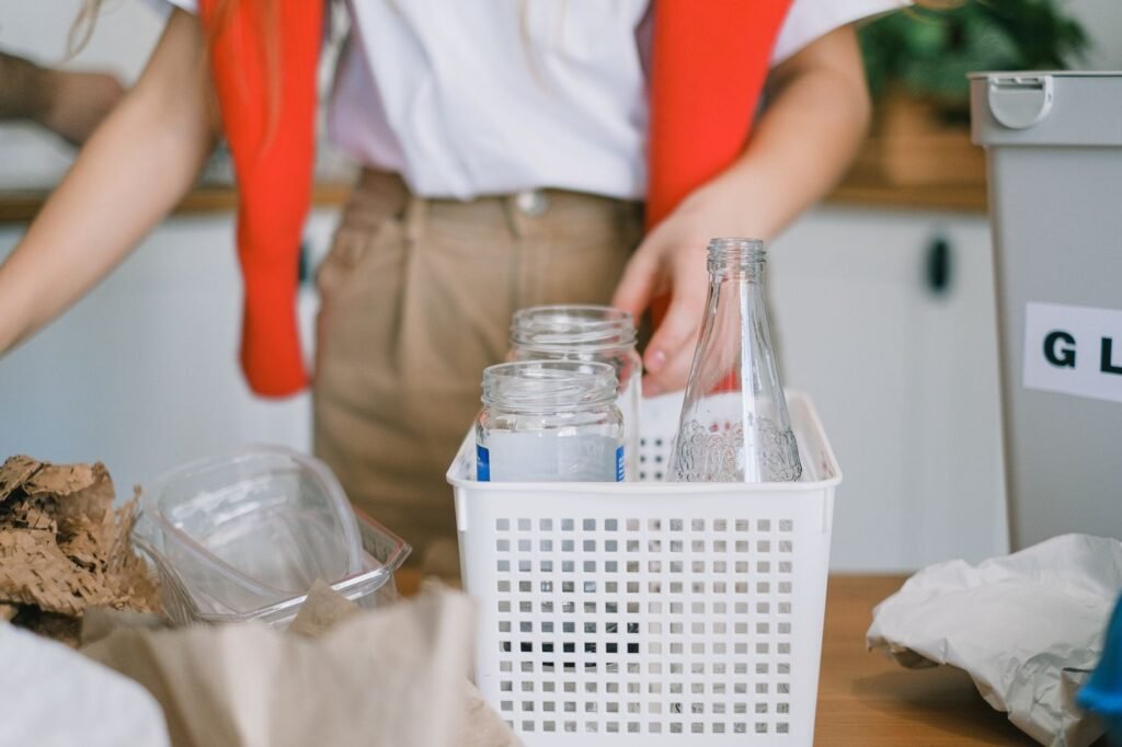 Woman sorting glass bottles into recycling containers at home