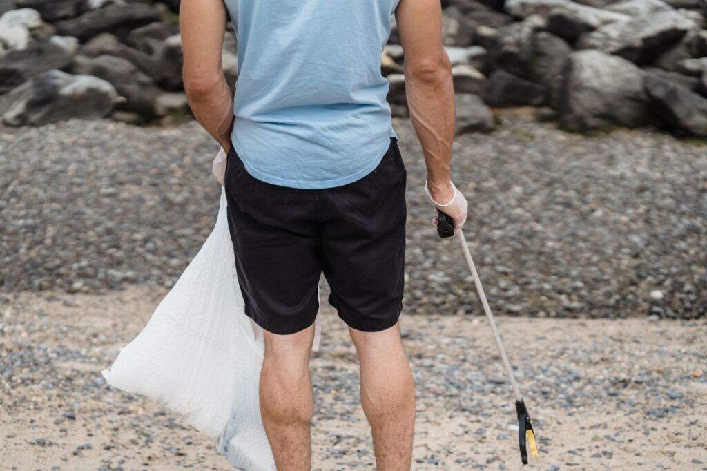 Man using a grabber tool to pick up plastic litter on a rocky beach
