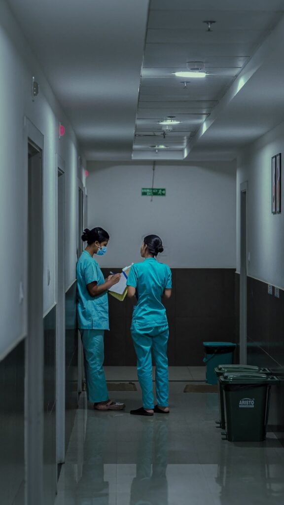 Two nurses in scrubs discussing patient notes in a hospital corridor