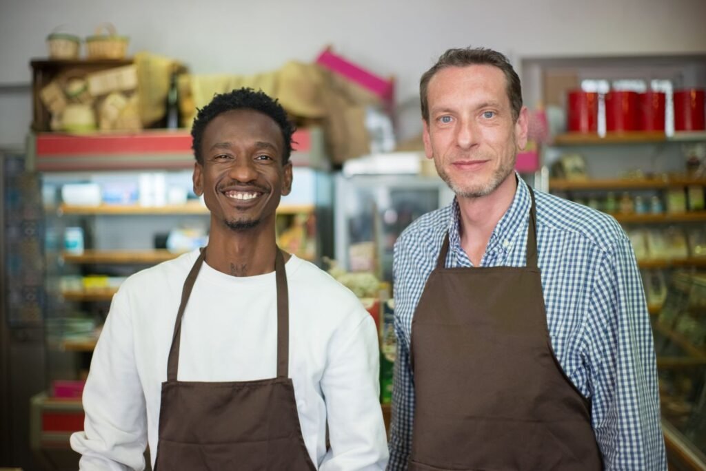 Two smiling shop owners in aprons standing in a grocery store