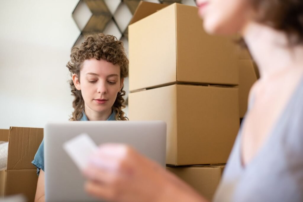 Two women sitting among cardboard boxes using a laptop to run an online shop