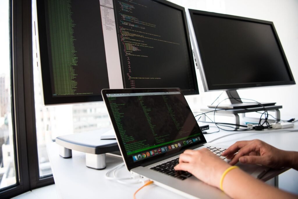Close-up of a person typing on a laptop in front of several monitors