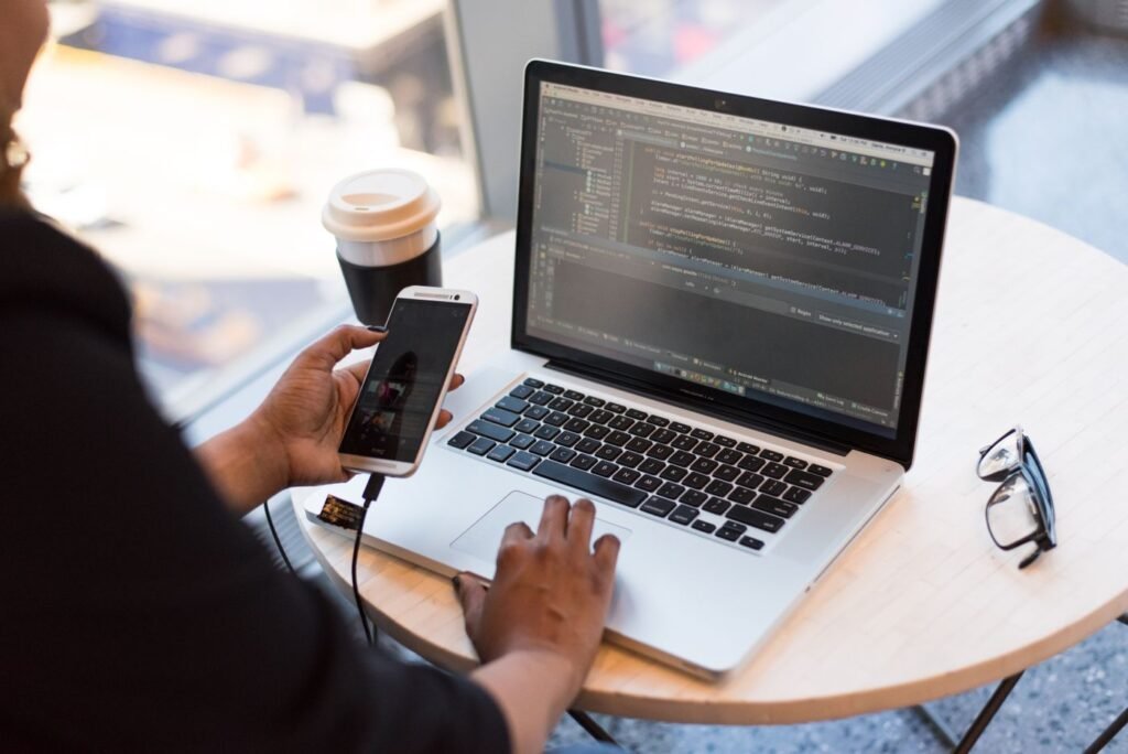 Person holding a smartphone while writing code on a laptop