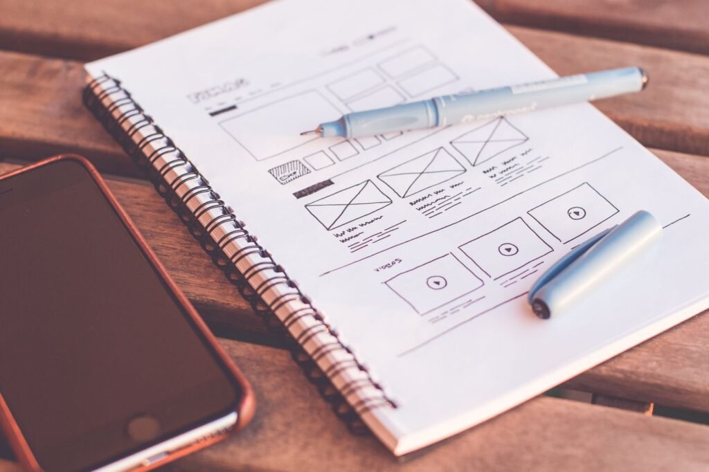Notebook with wireframe sketches next to a smartphone on a wooden desk