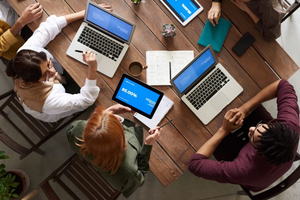 Group of people around a table reviewing plans on laptops and tablets