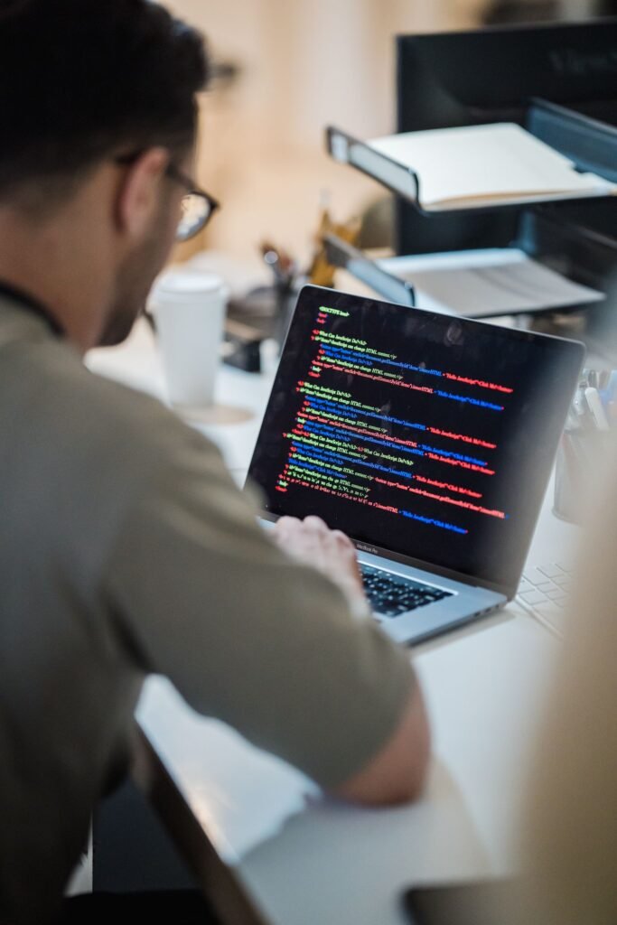 Man in a beige t-shirt looking at code on a laptop screen